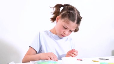 Genç kız derinden bilezik yapma sanatına odaklanmış. Canlı kil boncukları eşsiz kalıplara döküyor. Çalışma alanı çeşitli boncuklarla düzenlenmiş. Bu da nişanını gösteriyor.