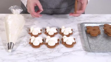 Zencefilli kurabiyeler mermer yüzeyde ikinci yarılarını beklerler, her biri lezzetli sandviçler yapmak için tereyağlı kremayla titizlikle borular. Boruların hassasiyeti şenlikli bir dokunuş katıyor..