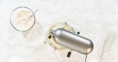 Klasik Şekerli Kurabiye Hamuru malzemeleri içeren elektrikli mikser ve kaselerin üst görüntüsü. Karıştırıcı kısmen karışık malzemelerle bir kasenin üzerine yerleştirilirken, yakındaki kaselerde un ve...