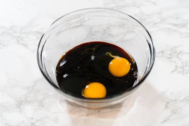 Yukardan aşağıya koyu pekmez ve cam bir kasede iki yumurta. Lezzetli Turuncu Zencefilli Kurabiye Kurabiyesi için ıslak malzemeler. Pekmez zencefilli çöreğe derinlik ve zengin bir renk katar..