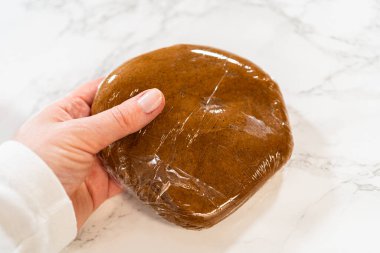 Elde tutulan plastik ambalaja sarılı bir porsiyon Baharatlı Zencefilli Kurabiye Dough Perfect. Hamur, lezzet ve dokuları geliştirmek için soğutulmaya hazır ve nazır..