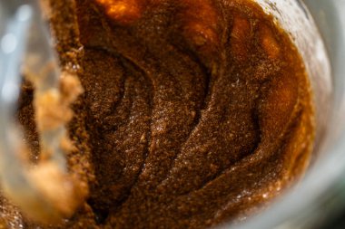 Karıştırıcı kasesinde kremalı tereyağı ve şekere eklenmiş koyu bir pekmez var. Pekmez entegre olmaya başlıyor, koyu kahverengi, aromatik bir karışım oluşturuyor..