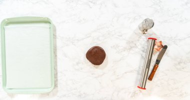 Beyaz mermer bir yüzey üzerinde boş bir yeşil kabartma çarşafı ve çikolata hamuru topu ve yakın pişirme araçları ile genel görünüm.