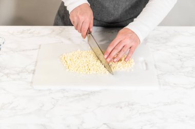 Beyaz bir kesme tahtasında, ustalıkla beyaz çikolata parçalarını bıçakla doğramak pişirme macerasına mükemmel bir dokunuş ekler..