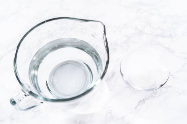 Cam ölçme bardakları suyla doludur, sıralanır ve dikkatli bir şekilde taze çilek yıkamada kullanılmaya hazırdır, kusursuz ve eksiksiz temizliği sağlar..