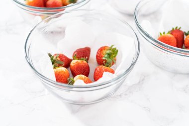 Parlak kırmızı çilekler, küf izleriyle karışmış, beyaz peçetedeki kağıt havluyla kaplı cam bir kasede dinleniyor, depolama tekniklerini gösteriyor..