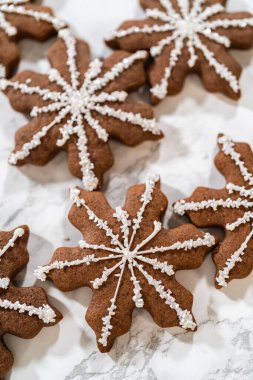 Çikolatalı, zencefilli, kar taneli kurabiyelerin detaylı görüntüsü kraliyet kreması ile süslenmiş, arka planda hafif düzenlenmiş, bayram kutlamaları için mükemmel..