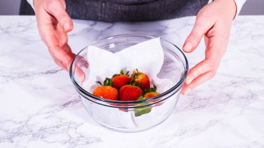 Çilekler, yeni yıkanmış ve kurutulmuş, cam bir kasede güzelce depolanmış kağıt havluyla kaplanmış ve tazeliği korumak için plastikle kaplanmış..