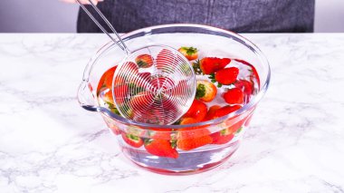 Olgun çilekler, depolama veya tüketimden önce temizlik ve uzun ömürlü olmak için meyveyi yıkamada bir adım olarak büyük bir bardakta karıştırma kabında suya gömülür..