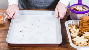 Beyaz kremalı kurabiyelerle dolu bayramlık zencefilli sandviç kurabiyelerinin yukarıdan görünüşü, çeşitli kesme kurabiyelerin olduğu tepsilerin yanında metal bir tepside düzgünce dizilmiş. Sahne tatil ruhunu yakalıyor.