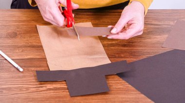 Adım adım. Öğretmen, kahverengi bir çantadan kağıt bir kukla yaparak, çalışma alanı olarak ahşap bir yüzey kullanarak çevrimiçi sınıfa rehberlik ediyor..