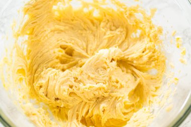 Cam bir kasede taze karışık limonlu kurabiye hamurunun yakın plan görüntüsü pürüzsüz ve tereyağlı dokusunu gözler önüne seriyor. Hamur taze limon lezzeti ve vanilya ile doludur.