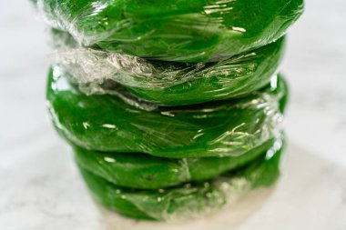 Yığılmış yeşil hamur parçaları, her biri plastik ambalaja sarılı, Dolapta soğutulmaya hazır canlı zencefilli kurabiyeler için.