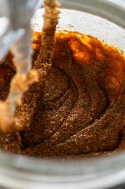 Karıştırıcı kasesinde kremalı tereyağı ve şekere eklenmiş koyu bir pekmez var. Pekmez entegre olmaya başlıyor, koyu kahverengi, aromatik bir karışım oluşturuyor..