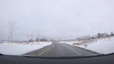 Denver, Colorado, ABD-26 Ocak 2024 - Sabah erken saatlerde yeni inşa edilmiş bir banliyö mahallesine sessiz bir sürüş getiriyor, yolu kaplayan taze kar ve karanlık bir gökyüzü altında evler.