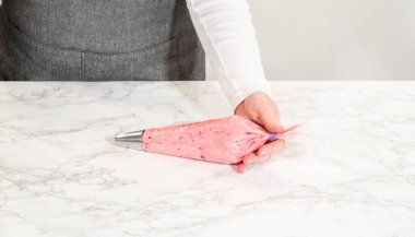 Limonlu kurabiyeleri süslemeye hazır içi canlı kızılcık kremasıyla dolu bir boru torbası. Bu zengin ve renkli tereyağı kreması limonlu kurabiyelere mükemmel bir tat katıyor.