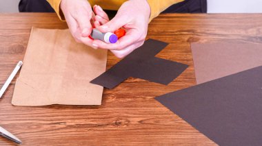 Adım adım. Öğretmen, kahverengi bir çantadan kağıt bir kukla yaparak, çalışma alanı olarak ahşap bir yüzey kullanarak çevrimiçi sınıfa rehberlik ediyor..