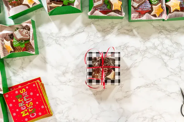 Noel kurabiyesinin hediye kutusunu saran, güzelce hazırlanmış Noel kutuları ile çevrili, tepeden tırnağa bir el resmi. Sahnede zencefilli kurabiye, şenlikli ambalajlar ve