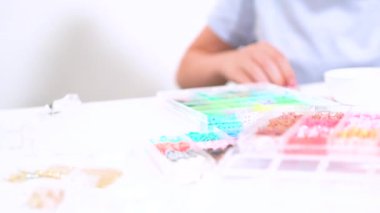 Genç kız derinden bilezik yapma sanatına odaklanmış. Canlı kil boncukları eşsiz kalıplara döküyor. Çalışma alanı çeşitli boncuklarla düzenlenmiş. Bu da nişanını gösteriyor.