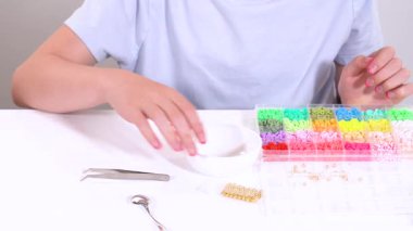 Genç kız derinden bilezik yapma sanatına odaklanmış. Canlı kil boncukları eşsiz kalıplara döküyor. Çalışma alanı çeşitli boncuklarla düzenlenmiş. Bu da nişanını gösteriyor.