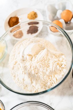 Arka planda ana zencefilli ekmek baharatları, tereyağı ve yumurtalarla dolu bir cam karıştırma kabının genel manzarası. Bu malzemeler klasik zencefilli çöreğin yapımında kullanılacak.