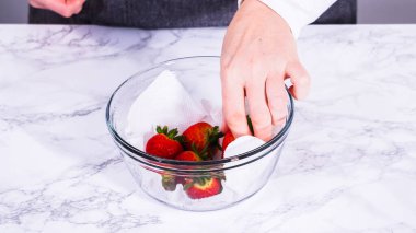 Çilekler, yeni yıkanmış ve kurutulmuş, cam bir kasede güzelce depolanmış kağıt havluyla kaplanmış ve tazeliği korumak için plastikle kaplanmış..