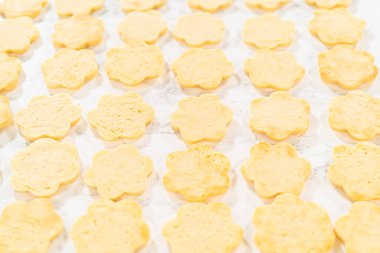 Paskalya Kurabiyesi Sandviçi için ahududu kreması ve ahududu kremalı sandviçle doldurulmaya hazır, parşömen üzerine serilmiş çiçek şeklinde sıralanmış şeker kurabiyeleri. Adım adım tarif etmek için harika.