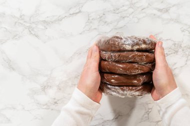 Plastiğe sarılı soluk zencefilli hamur mermileri tutan eller incelikli baharatlı kurabiyeler için. Hamur mermileri soğutulmaya ve güzelce istiflenmeye hazır.
