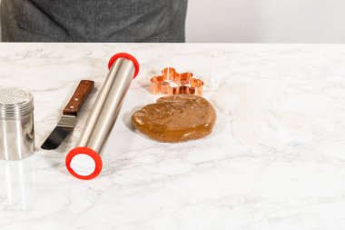 Fırın aletleri ve yuvarlak bir top zencefilli ekmek hamuru yuvarlanmaya hazır. Aletler arasında mermer bir yüzeye yerleştirilmiş merdane iğnesi, kurabiye keskisi ve un kabı yer alıyor..