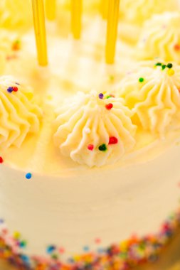 Donmuş kekin dikey yakın çekimi sarı mumlar ve üzerine renkli yuvarlak serpiştirilmiş vanilyalı girdaplar gösteriyor. Pastanın yüzeyi pürüzsüzdür. Şekerlemelerde görünür bir doku ve...