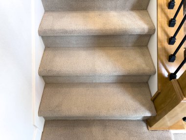 Alt basamakların yakın plan bej halılı merdiven, ahşap ve demir parmaklıklar, gösterişli doku ve işçilik. İç tasarım veya döşeme projeleri için kullanışlı.