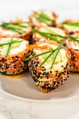 Tabakta servis edilen füme somon soslu krem peynirli rulo. Ekmekler taze soğanla eşit şekilde süslenmiş ve çıtır çıtır susam tohumlu kaplama içeriyor. Bu yemek mükemmel.