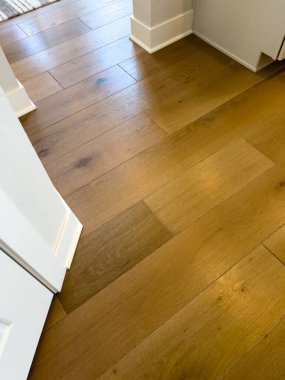 Beyaz dolaplar ve süpürgeliklerle çevrili mutfak koridorundan geçen doğal meşe ağacı zemininin manzarası. Güneş ışığı tahtalardan yansıyarak tahılları ve sıcak tonlarını arttırır. İdeal