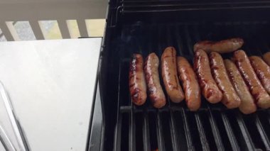 Ağır çekimde sosisler barbeküde ızgara yapar, bir sosis de açıyla döner. Duman yükselir ve sahne sosisler arasında hafif pişirme farklılıklarını gösterir. Doğal ve samimi bir ızgara.