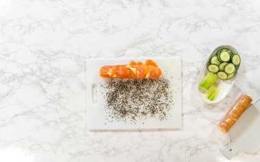 Krem peynir, salatalık ve kereviz ile hazırlanmış dilimlenmemiş somon rulosu üzerine susam tohumu serpiştirilmiş beyaz bir tahta. Mermer tezgahta gösteriliyor.