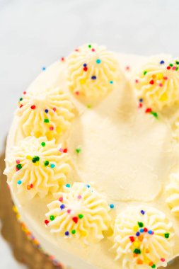 Üzerinde tek parça vanilya şekerlemesi olan beyaz bir kekin genel görüntüsü. Her bir krema kıvrımı çok renkli parantez dışı şekillerle süslenmiş. Pasta çerçevenin ortasında.