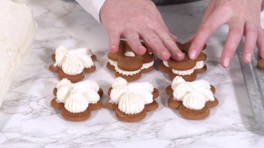 Zencefilli kurabiyeler mermer yüzeyde ikinci yarılarını beklerler, her biri lezzetli sandviçler yapmak için tereyağlı kremayla titizlikle borular. Boruların hassasiyeti şenlikli bir dokunuş katıyor..