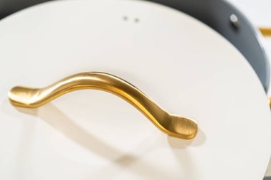 Minimalist fotoğraf, mat beyaz tencere kapağındaki altın sapı gösteriyor. Stok ürün gösterimleri, mutfak reklamları veya katalog ekleri için tasarlandı.