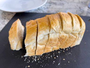 Siyah bir kesme tahtasına sergilenen iki dilim ekmek. Ekmek pürüzsüz kenarlarla kesilmiş. Yumuşak ve havadar içini gösteriyor. Kırıntılar çevredeki yüzeyi doğal ışıkla dağıtır..