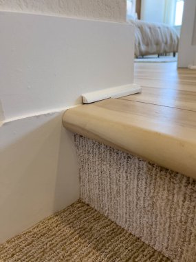 Merdivenin tepesindeki ahşap ve beyaz dikey merdiven balyalarıyla çerçevelenmiş desenli beyaz bir duvarın yakın plan görüntüsü. Mimari detaylar ya da emlak tasvirleri için ideal.