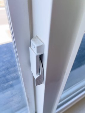 Sürgülü pencere çerçevesindeki beyaz bir pencerenin kilidini kapat. Temiz yüzey ve basit mekanizma doğal gün ışığında görülebilir..