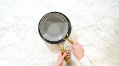 İki el, modern gri seramik tavayı beyaz mermer bir tezgaha yerleştirirken görülüyor, hem tavanın hem de yüzeyin dokusunu vurguluyor..