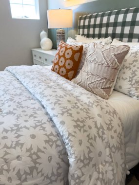 Beyaz ve gri çiçekli yorgan ve parlak dekoratif yastıklı şık bir yatak odası tasarımı. Perakende mobilya pazarlama ya da dijital durum panoları için harika..