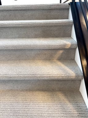 Her iki tarafında bej halı ve siyah metal parmaklıklar olan modern bir merdivenin simetrik ön görünüşü.