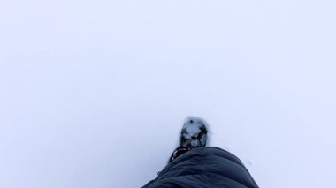 Manzara, karla kaplı bir zemine doğru iniyor. Kışlık bir pantolonun içinde tek bir bacak öne eğiliyor ve el değmemiş karda yol açıyor. Koyu beyazlık her şeyi sarıyor.