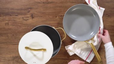 Altın saplı ve beyaz kapaklı şık tencere ve tavalar kırsal bir ahşap masaya nazikçe yerleştiriliyor. Sahne temiz, modern bir mutfak estetiği yakalıyor, vitrin için ideal.