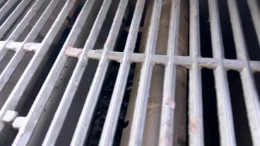 Açık hava gaz ızgarası kapağı açık temizleniyor, etrafı temizlik aletleri ve verandada bir şişe temizleyici ile çevrili. Kurulum, barbekü ekipmanlarını önceden korumanın önemini vurguluyor