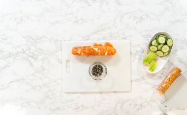 Tütsülenmiş somon bloğu, yanında krem peynir, salatalık kurdelesi ve siyah-beyaz susam tohumları olan bir kesim tahtasının üzerine kurulmuştur..