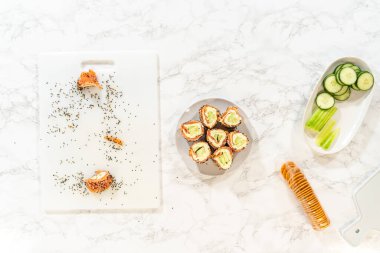 Dilimlenmiş somon krem peynirli rulo. Susam tohumlarıyla kaplı. Tertemiz beyaz bir kesim tahtasında servis ediliyor..