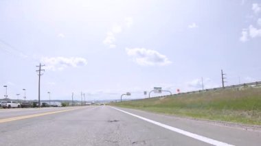 Parker, Colorado, ABD-30 Mayıs 2025 - Araçlar otobanda sağda çimenli bir tepe ve solda yol kenarındaki işletmeler ile ilerliyor. Birkaç dağınık bulutla hava güneşli..